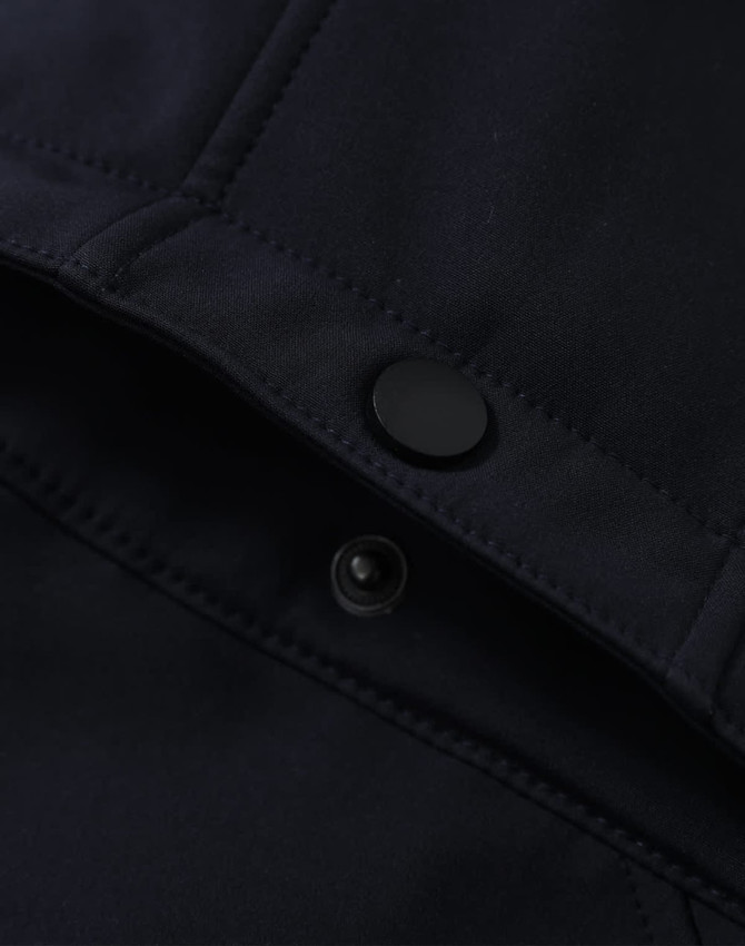 A close-up of a navy softshell jacket featuring a snap button and interior stitching details.