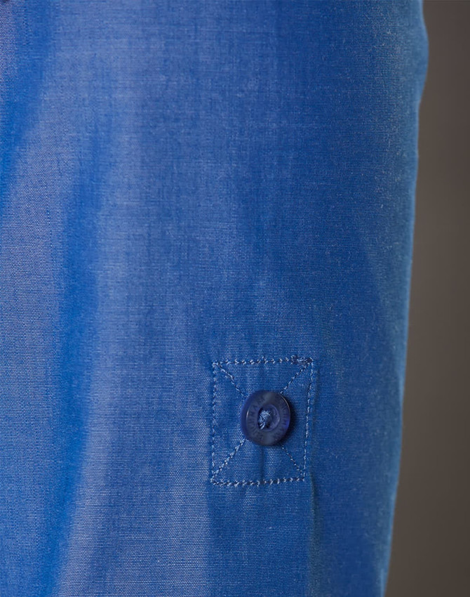 A close-up of a blue women's shirt featuring a button and a rolled-up sleeve. The fabric has a subtle texture.