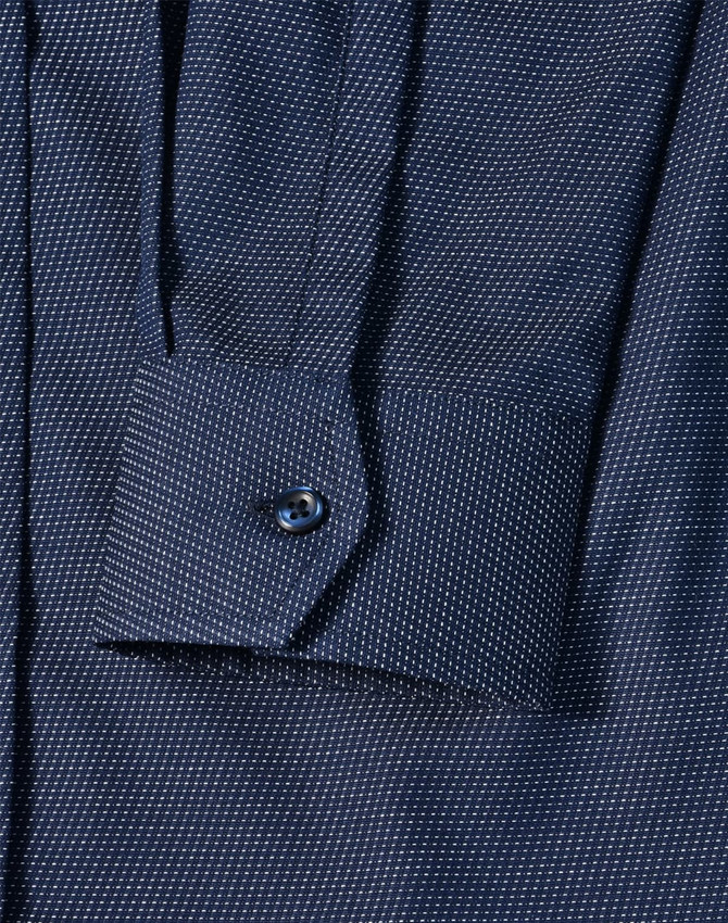 A navy blue pin dot stretch long sleeve shirt with a buttoned cuff and a branded logo.