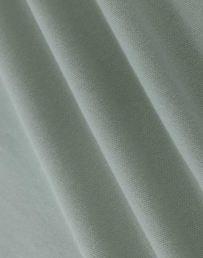 A close-up of light green cotton fabric with a smooth texture, showcasing fine weaves and folds.