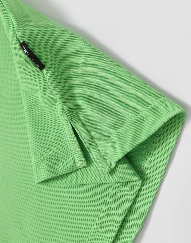 A green polo shirt featuring a logo and a textured fabric. Close-up of the collar and sleeve hem.
