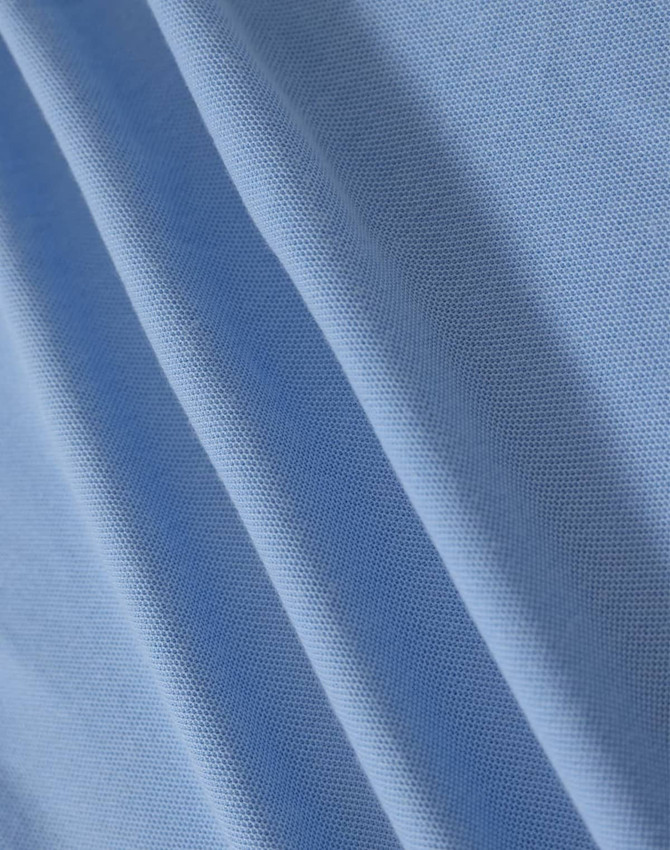 A close-up of light blue fabric with a textured surface, suitable for polo shirts. It has a branding logo.