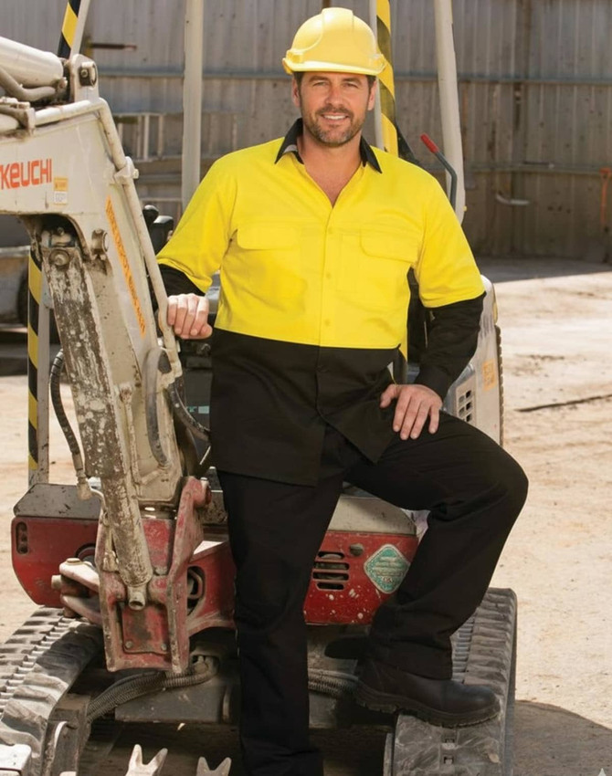 A man wearing a bright yellow and black long-sleeve safety shirt stands beside construction equipment. The shirt features a logo.