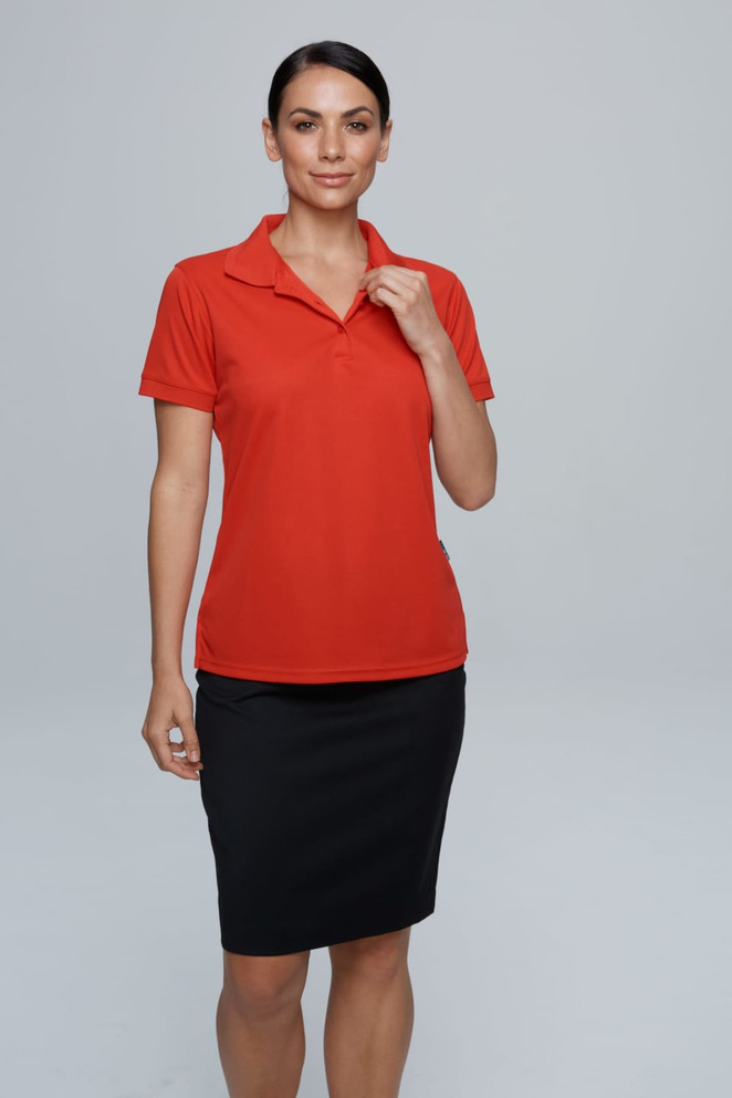 A model wearing a red polo shirt paired with a black skirt, showcasing the "LACHLAN LADY POLOS RUNOUT" product.