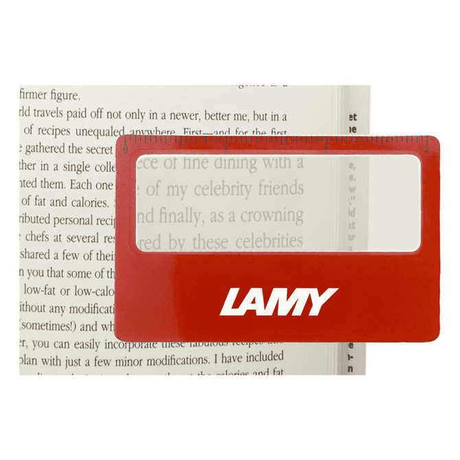 A red pocket ruler magnifier with a clear lens, placed over text in a book, featuring a logo.