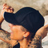 A black cap with a curved brim, worn by a person with tattoos, showcasing a side view. A black cap with a curved brim, worn by a person with tattoos, showcasing a side view.