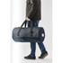 A person carrying a navy waterproof duffel bag with black straps and a branding logo.