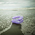 A purple inflatable chair rests on wet sand by the ocean, with waves gently lapping nearby.