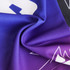 A vibrant scarf featuring a mix of purple and blue patterns, showcasing a smooth, textured fabric. It has a logo.