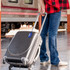 A person holds a black suitcase with a blue coloured silicone luggage tag attached, standing at a train station.