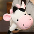 A cow hand puppet in black and white, with pink ears and a round face, held by a person.