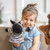 A zebra hand puppet in black and white is being held by a smiling child wearing a blue dress.