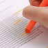 A hand holding an orange highlighter crayon, highlighting text on a sheet of paper.