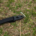 A black strap with a metal anchor pin on grass, designed for securing outdoor equipment.