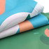 A folded outdoor blanket featuring a vibrant design with blue, green, and peach colours, along with a logo.
