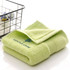 A folded green embroidered cotton hand towel displayed next to a wire basket. The towel features a logo.
