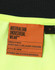 A label from a high-visibility yellow safety polo shirt featuring orange text and a black background.