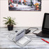A grey electronic accessory organiser bag with multiple compartments, displayed on a desk alongside a laptop and a plant.