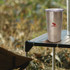 A drink bottle made of stainless steel with a shiny finish, featuring a logo, placed on a camping table outdoors.