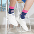 A pair of socks in navy blue with pink accents and a floral pattern, worn with white sneakers. A pair of socks in navy blue with pink accents and a floral pattern, worn with white sneakers.