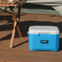 A blue and white 6L cooler box with a logo, placed on a wooden deck near a folding table.