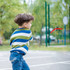 A child in a striped blue and green shirt throws a red V-shaped boomerang toy outdoors.