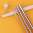 A set of four stainless steel drinking straws with a cleaning brush and a beige carrying case, on a yellow background.