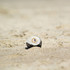 A white and black Hacky Sack is resting on a sandy surface, featuring a logo on its front.