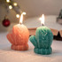 Glove-shaped candles in orange and teal with flames, set against a softly lit background and a book.