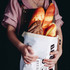 A linen bread bag in white, filled with various types of bread, held by a person in a pink shirt. A linen bread bag in white, filled with various types of bread, held by a person in a pink shirt.
