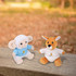 Two plush toys: a sheep in a blue shirt and a kangaroo in a white shirt, both with branding, set in a natural outdoor setting.