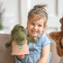 A green crocodile hand puppet held by a smiling child, wearing a light blue dress and a tiara.