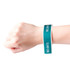 A hand wearing a teal disposable Tyvek wristband with a white interior, featuring a simple logo. A hand wearing a teal disposable Tyvek wristband with a white interior, featuring a simple logo.