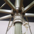 A close-up of a green patio umbrella's support structure and pulley system, featuring a central joint and connecting ropes.