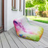 An inflatable lounge chair in a rainbow gradient design, placed on a wooden deck outside. It has a logo on the side.