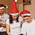Three individuals wearing red Santa hats with white trim, engaging in a festive activity. One hat features a logo.