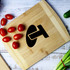 A bamboo cutting board displaying a logo, with cherry tomatoes and chopped spring onions alongside it.