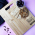 A bamboo chopping board featuring a handle, with crackers and olives displayed on top. The board has a logo.