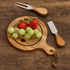 A wooden cheeseboard featuring strawberries and green grapes, with a knife and fork made of wood and metal.