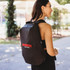 A black backpack with a logo, worn by a woman outdoors. The design is sleek and modern.