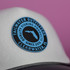 A white trucker cap with a black visor featuring a round blue logo on the front.