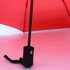 A red umbrella with a black handle and strap, featuring a logo on the handle.