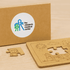 A natural wood jigsaw puzzle set with a puzzle piece and a brown box featuring a logo.