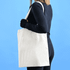 A person holds a plain white calico tote bag against a blue background. The bag features a simple design and has a logo.