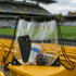 A transparent drawstring bag with black accents, containing a phone, sunscreen, keys, and a small box, sits on a stadium seat.