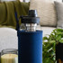 A drink bottle with a glass body, black lid, and navy blue insulated sleeve. It features a built-in tea infuser.