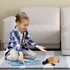 A plush platypus toy in brown and beige, with a child playing on a rug in a modern living room setting.