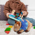 A plush wombat toy with a blue shirt sits on a soft surface, beside a child playing with colourful blocks.