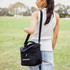 A black cooler bag with a shoulder strap and mesh pocket, being carried by a person in a casual outfit.