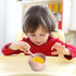 A silicone suction bowl in pink filled with corn, positioned in front of a child with a spoon.